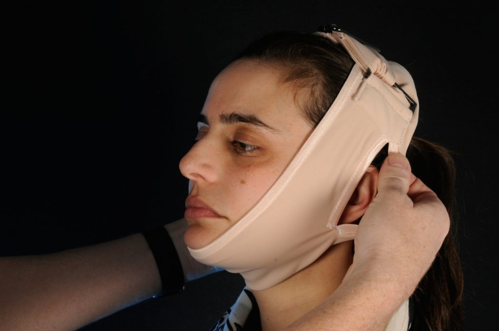 A patient wearing a supportive facemask after surgery